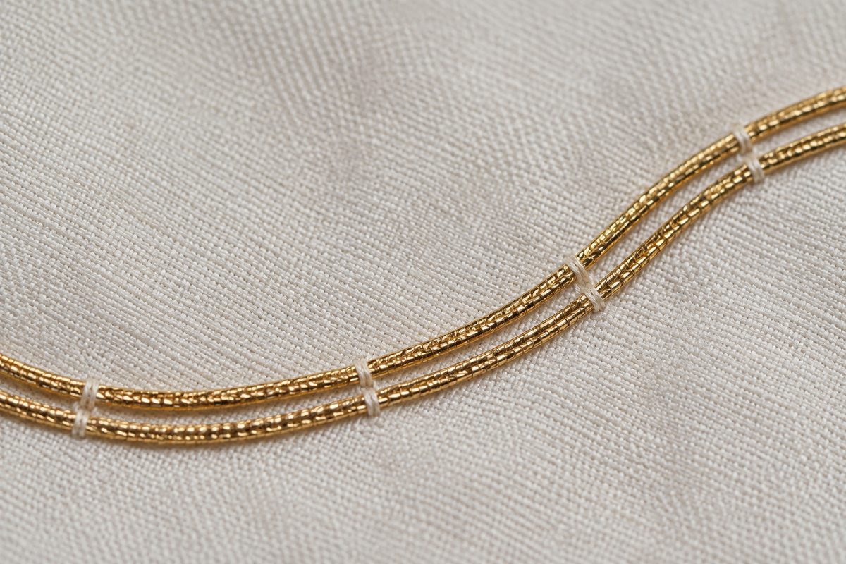 Fine stitches hold paired gold-colored threads against ivory cloth.