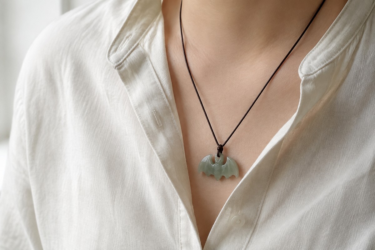 Small green bat pendant on a cord at an adult’s neckline beside an ivory linen shirt.
