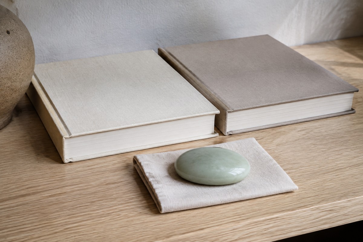 Two plain clothbound books behind a pale green stone on a folded linen square.