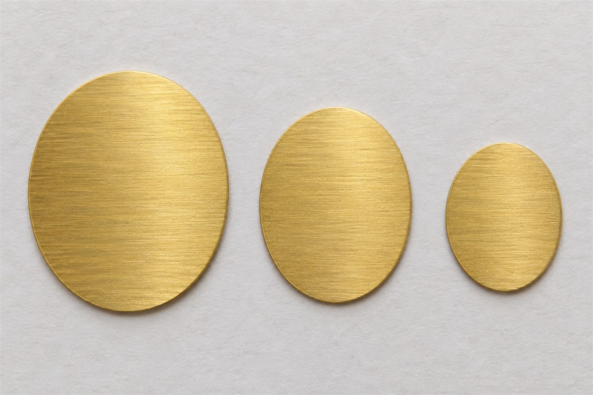 Three solid oval metal shapes of decreasing size lying on pale paper.