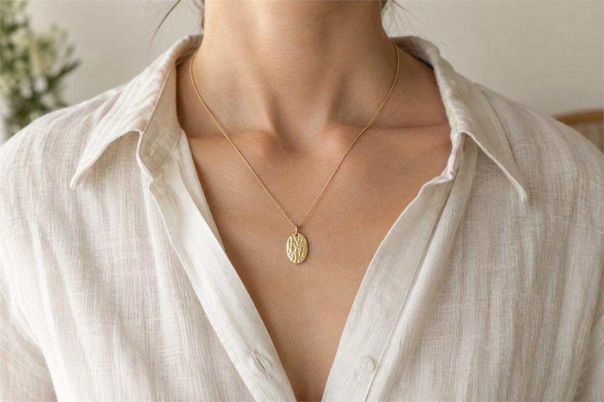 Small textured oval pendant worn on a fine chain with an ivory linen shirt.