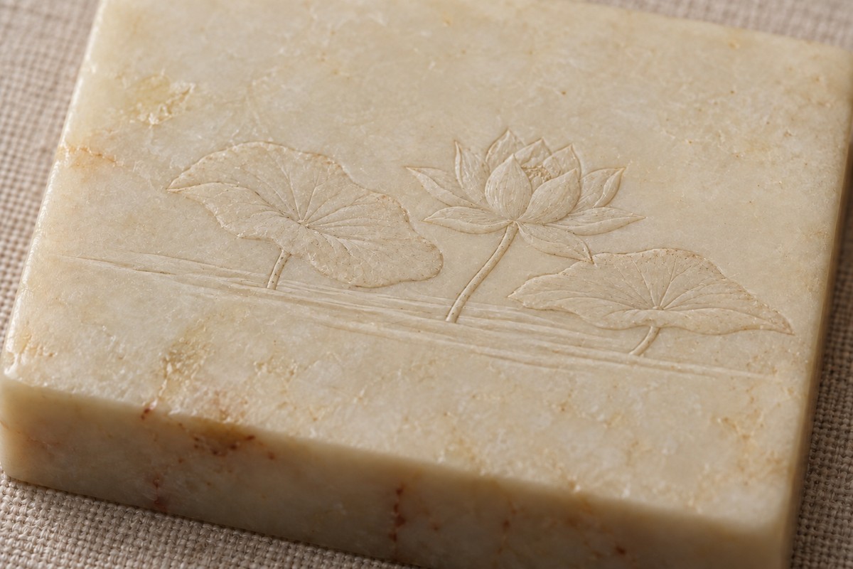A lotus flower and broad leaves rise above smooth ground on pale stone.