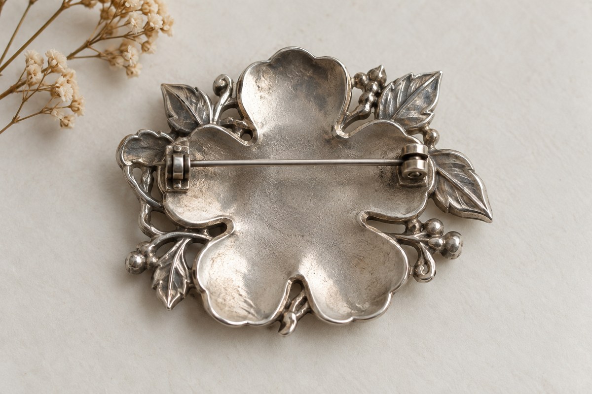 Back of a silver-colored brooch showing its pin, clasp, and attachment points.