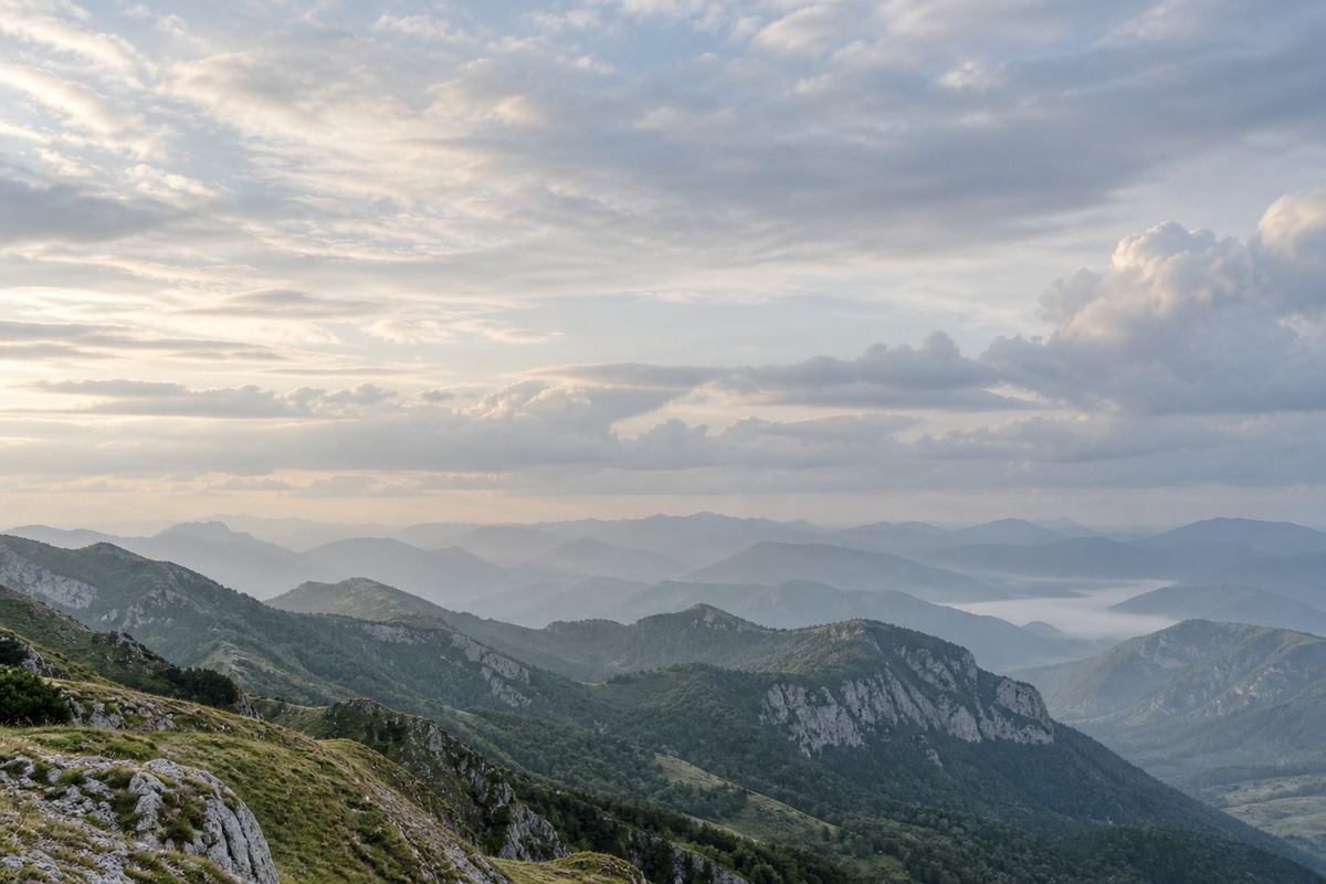 Soft clouds above layered mountain ridges beneath a pale, expansive sky.