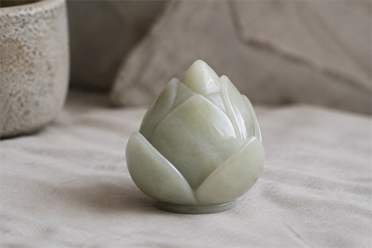 A small three-dimensional pale jade lotus bud resting on linen.