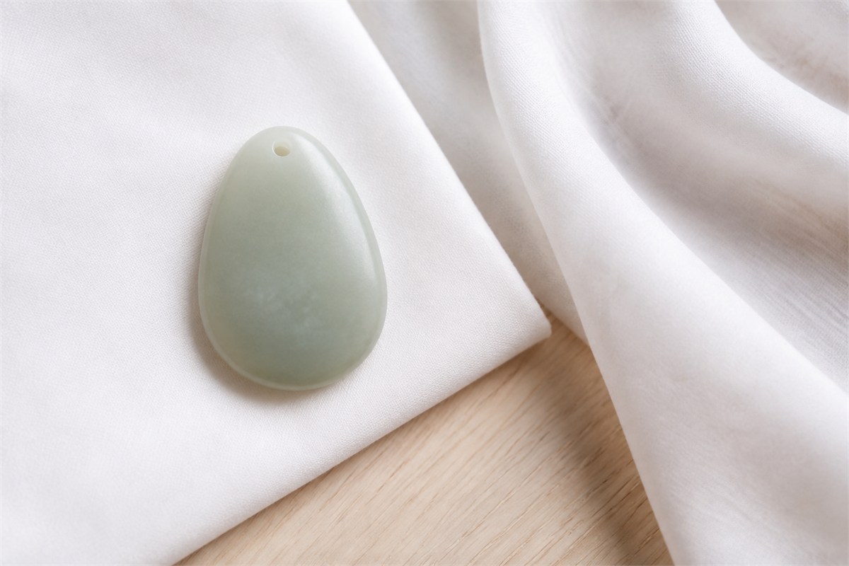 A pale jade pendant resting beside a folded soft white cloth.