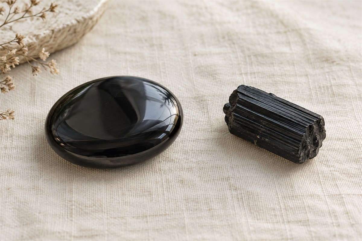 A smooth black obsidian stone beside a striated black tourmaline crystal.