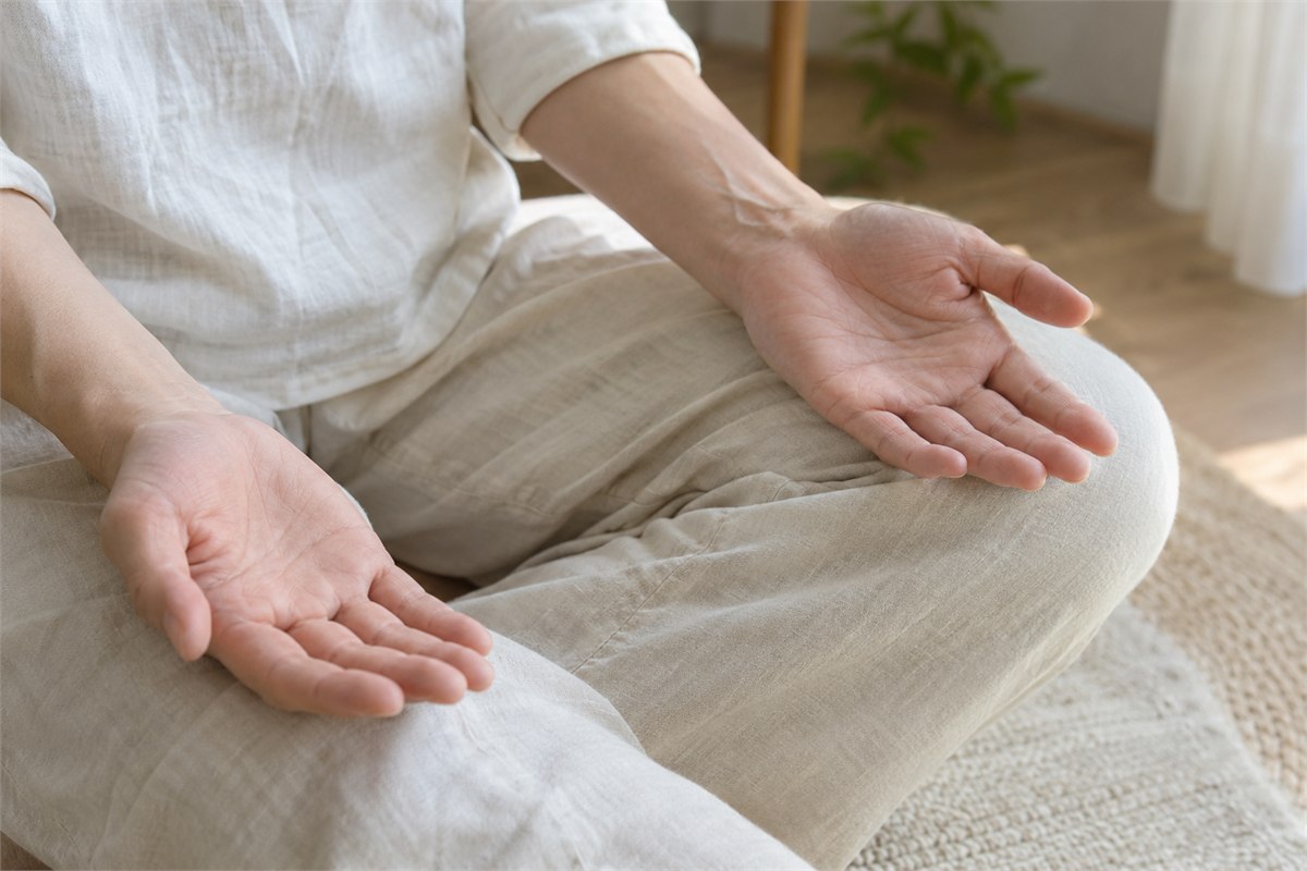 Relaxed open hands resting on a seated adult’s knees.