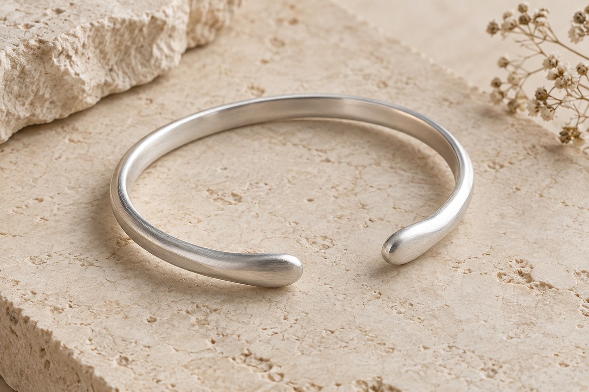 An oval silver cuff with a modest opening and smooth rounded ends on a pale stone ledge.