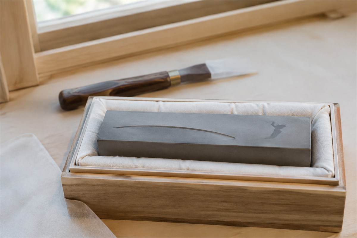 Curved recessed line and faint brush mark on a gray practice stone in a padded wooden tray.