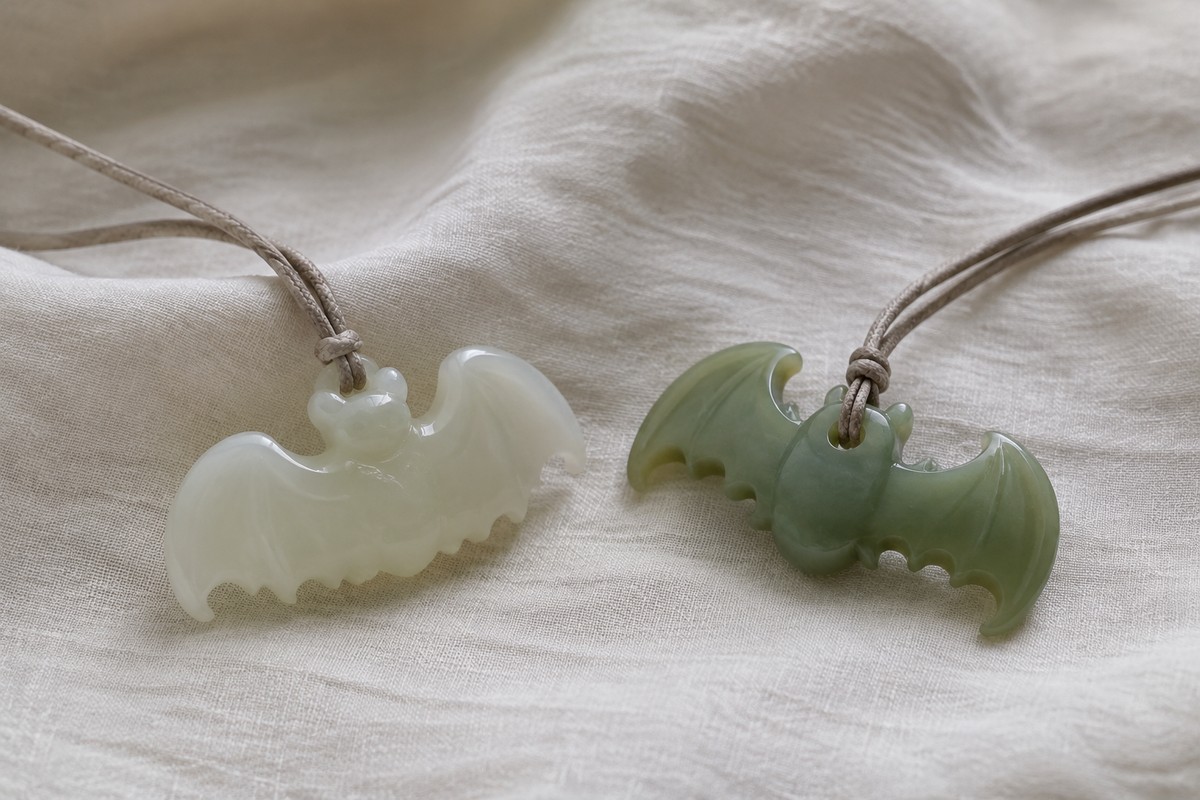 A white bat pendant and a green bat pendant on separate folds of linen.