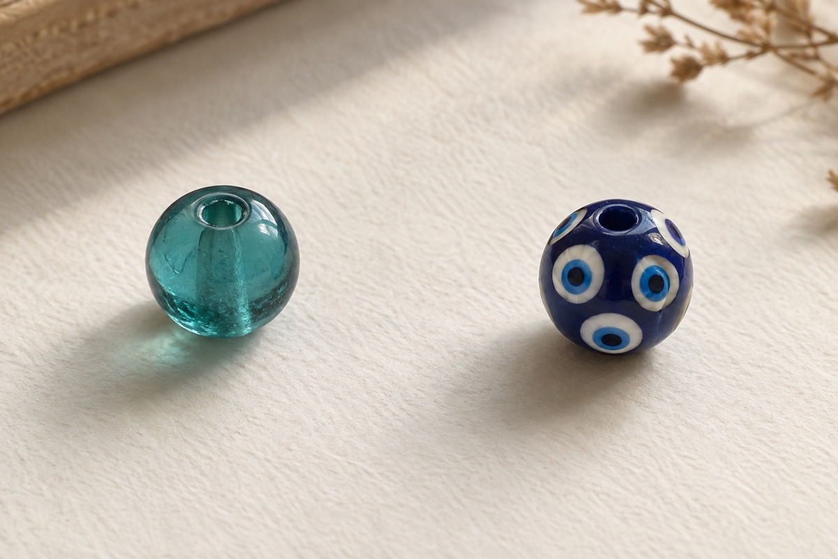 Plain translucent teal bead beside a blue bead decorated with cream and blue concentric eyes.