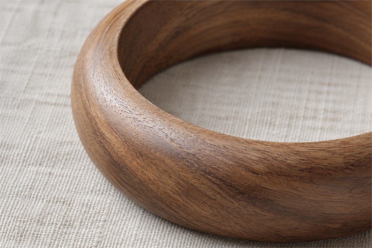 Close view of fine brown wood grain across the curved surface of an uncarved bangle.