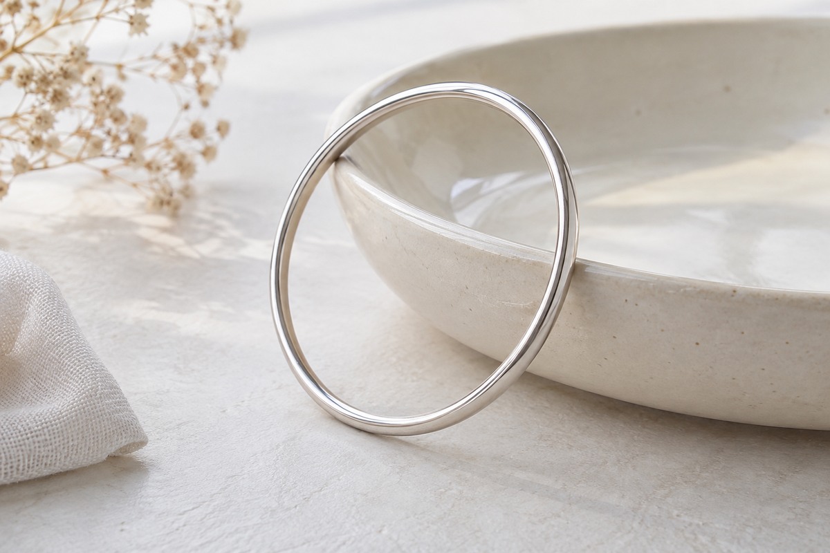 A polished silver bangle leaning against a cream ceramic dish.