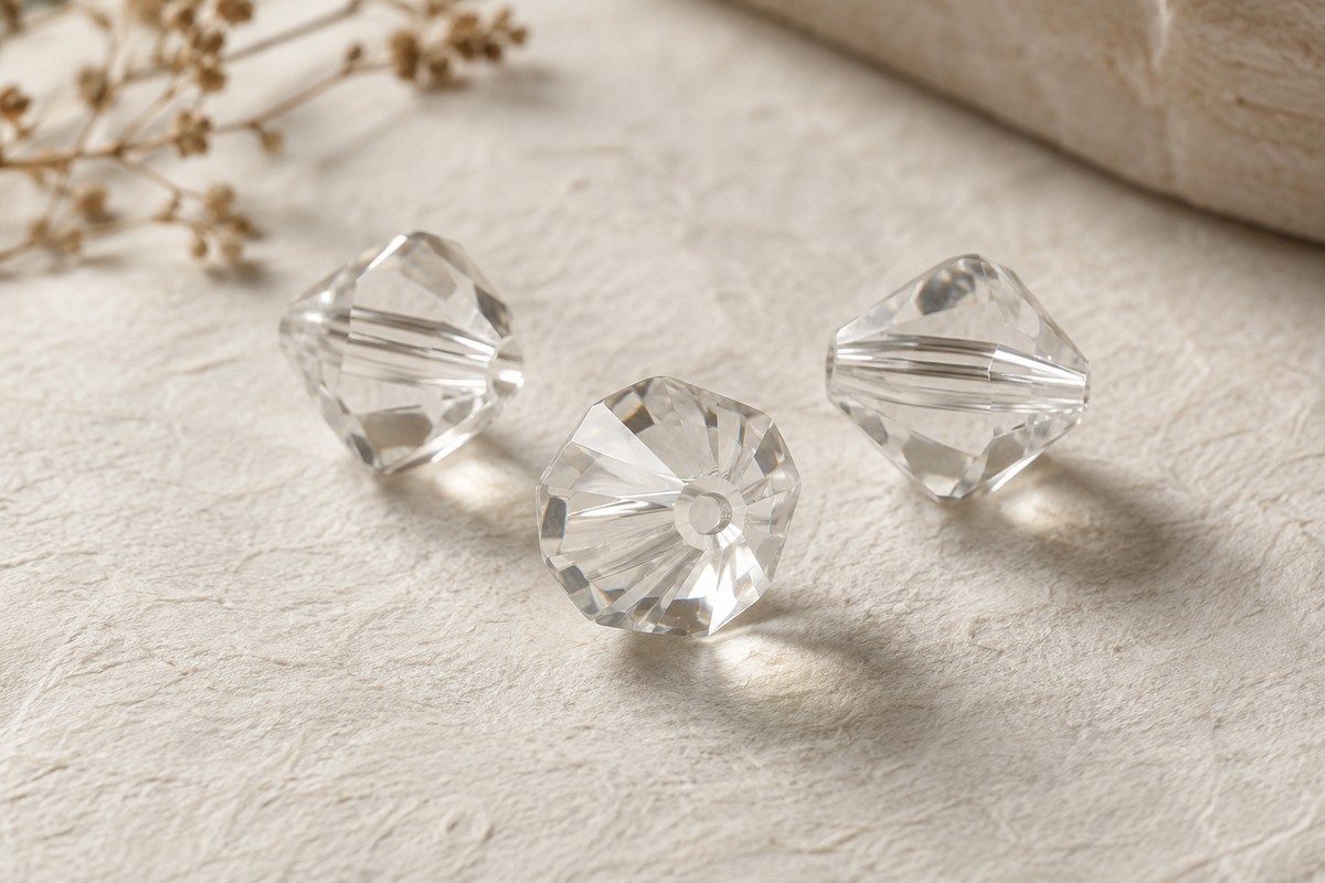 Three colorless faceted glass beads with visible threading holes on ivory paper.