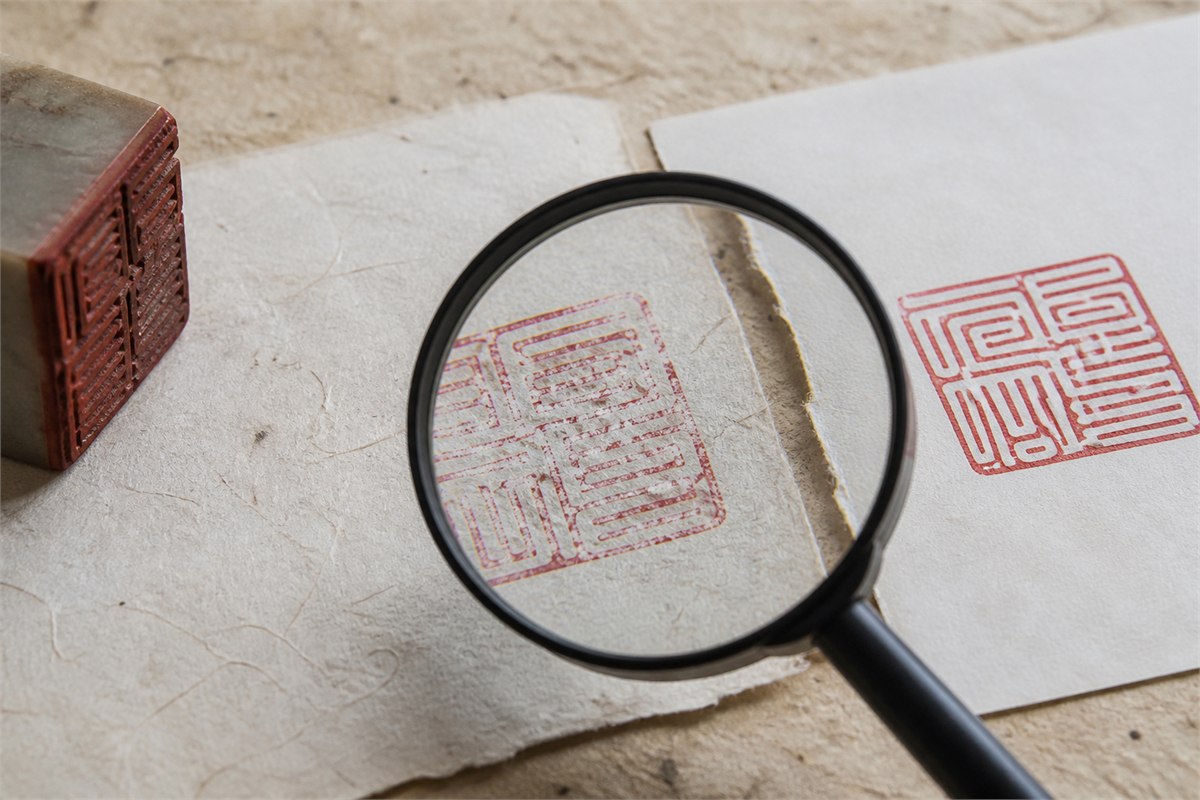 Magnifying glass over a worn red seal impression on textured paper