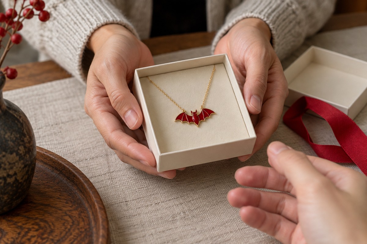 Hands offer an ivory gift box containing a red bat pendant.