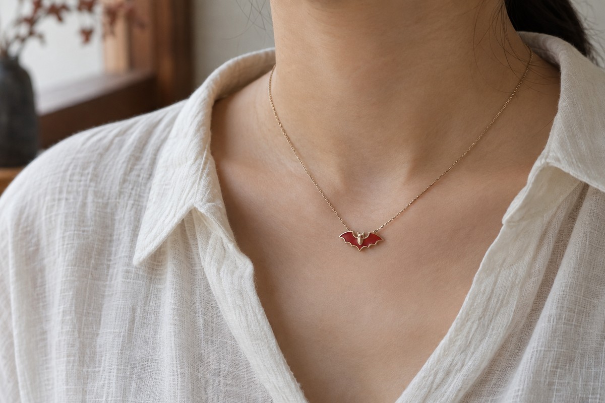 A small red bat pendant worn over an ivory shirt.