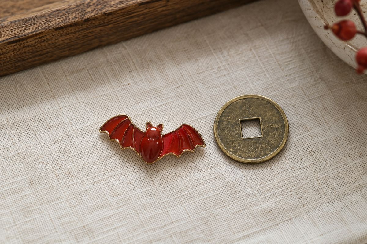 A red enamel bat sits beside a round brass coin charm with a square opening.
