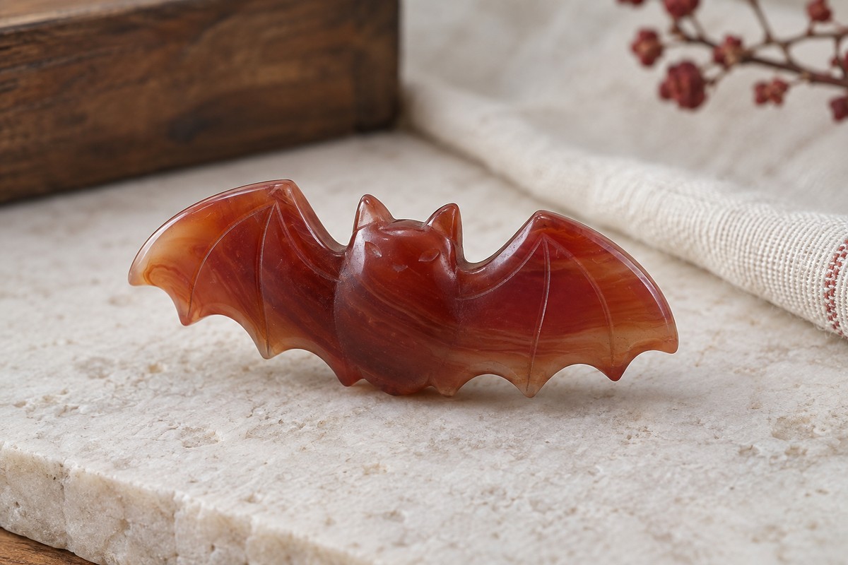 A polished red stone bat carving rests on a pale stone surface.