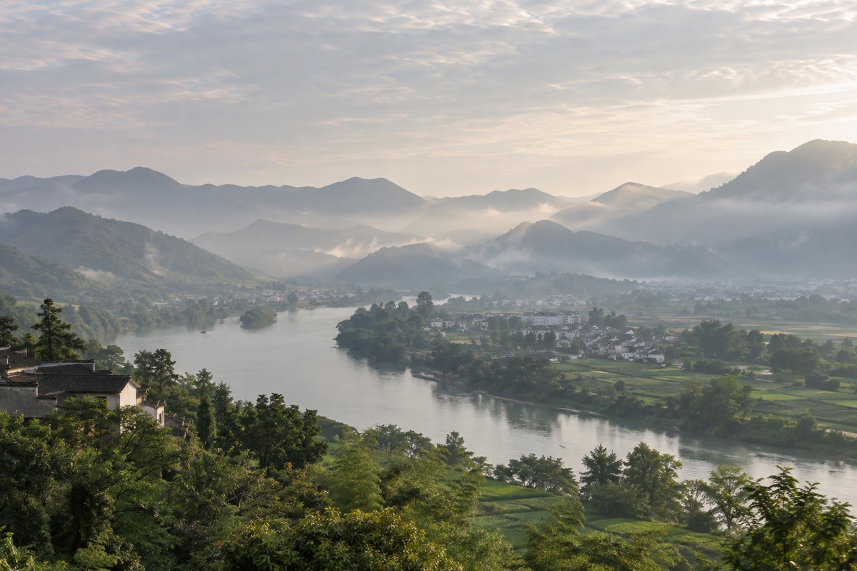 A broad river curves between low mountains and a quiet settlement.