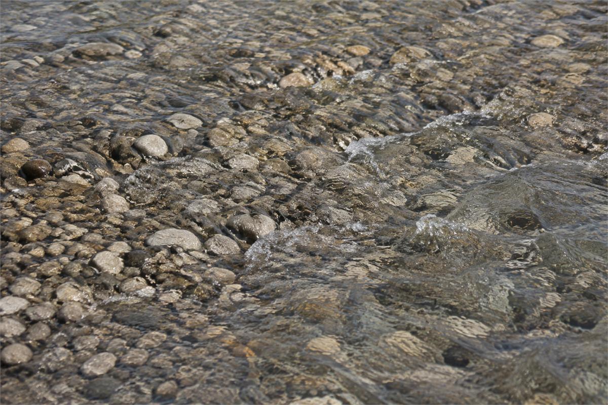 Clear shallow water flowing around rounded gravel on a riverbank.