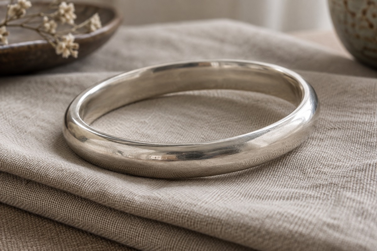 A substantial rounded silver bangle resting on folded oatmeal linen.