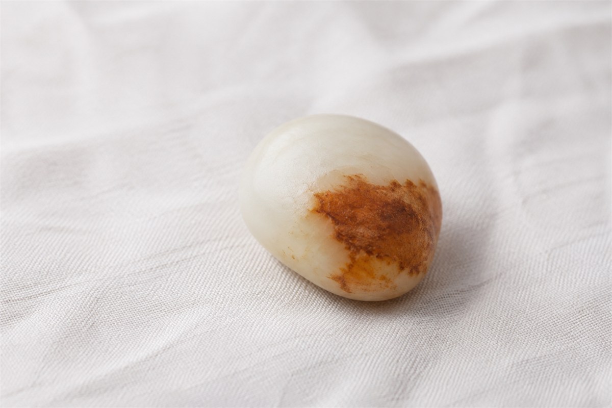 Cream-colored rounded stone with a russet patch on pale linen.