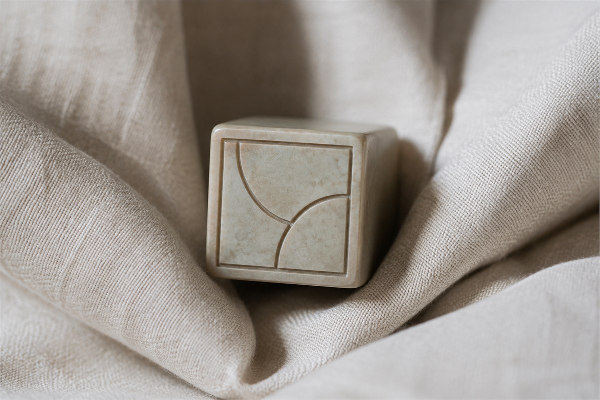Square practice seal face with a recessed border and two curved grooves, supported by linen.
