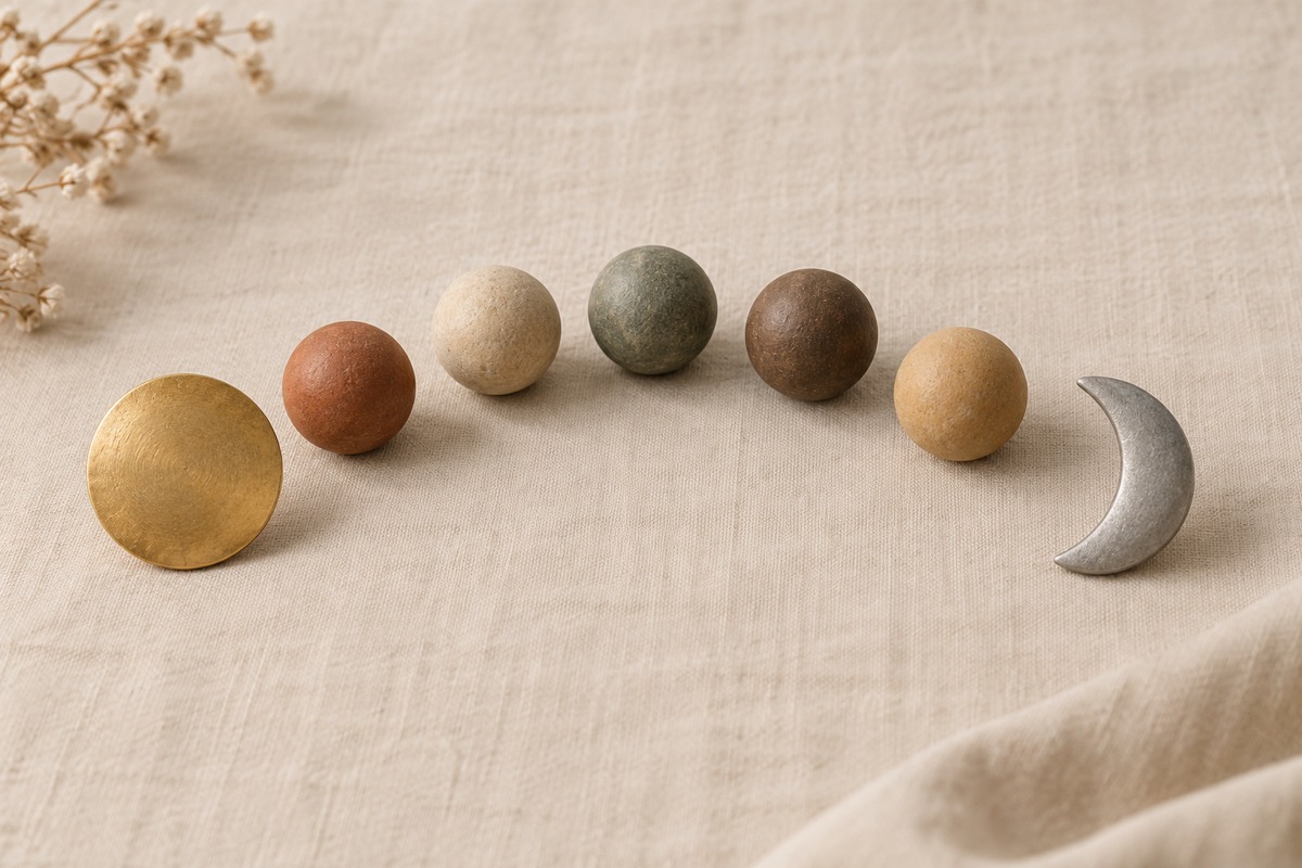 A sun disc, crescent moon and five small spherical forms rest on pale linen.