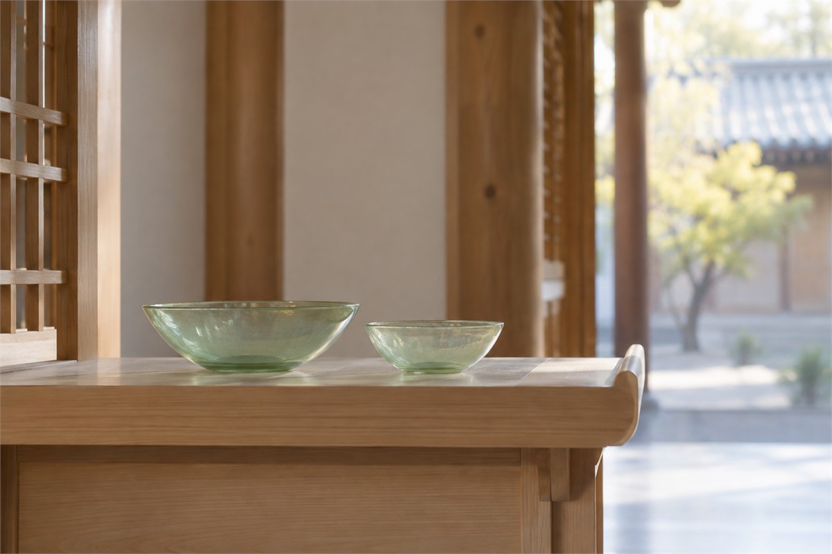 Two pale green glass bowls on a wooden shelf beside an open courtyard.
