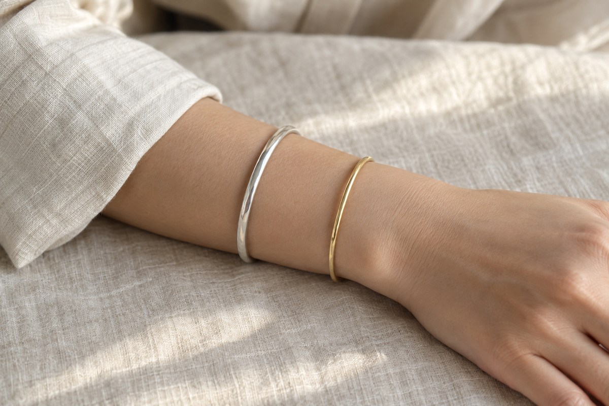 A silver bangle and a slender gold bangle worn with space between them on an adult forearm.