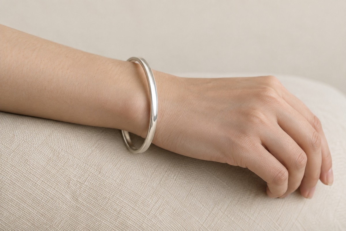 A loosely fitting oval silver bangle on an adult wrist with relaxed fingers.
