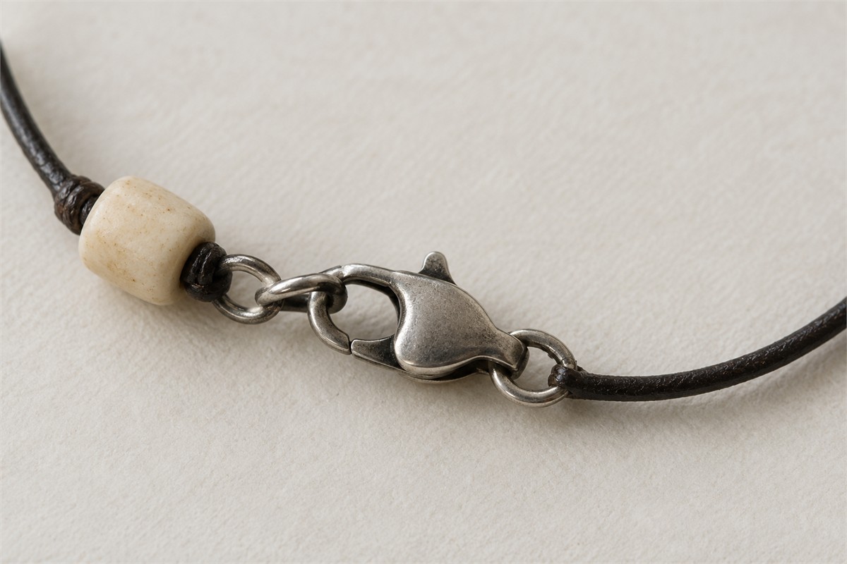 Silver-colored clasp with dark recesses beside a pale bead and cord.