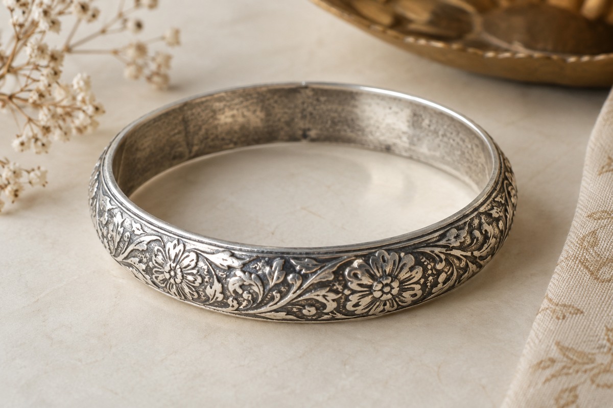 A worn silver bangle with subtle gray patina and fine surface marks on neutral paper.