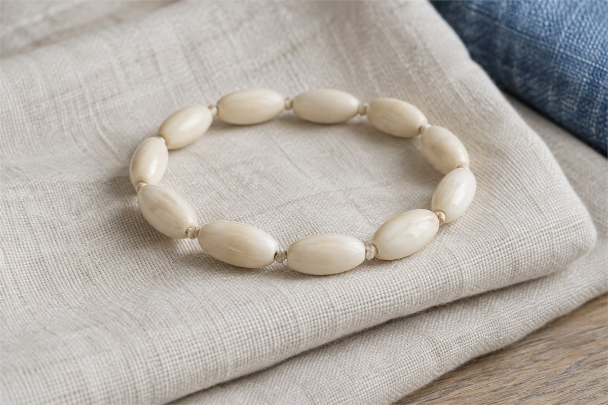 A cream bead bracelet beside a folded linen sleeve and denim fabric.