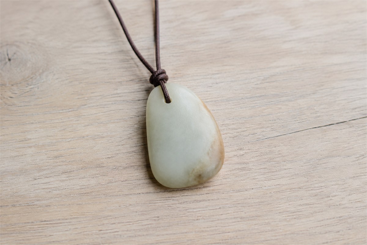 A rounded pale pendant with a small drilled hole and brown cord.