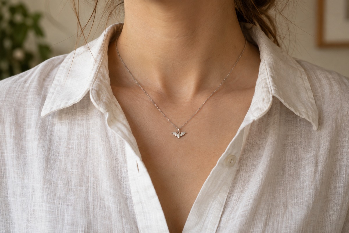 Tiny silver-colored bat pendant on a fine chain worn with a white linen shirt