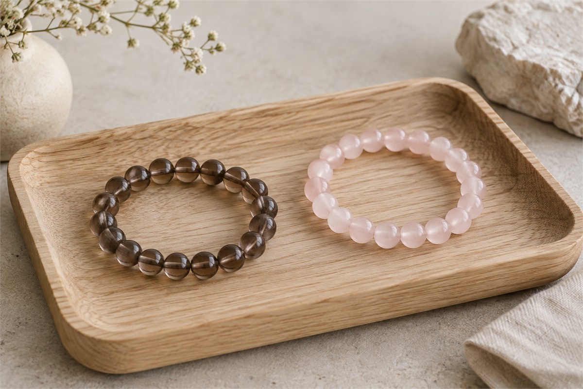 Smoky quartz and rose quartz bead bracelets resting apart on an oak tray.
