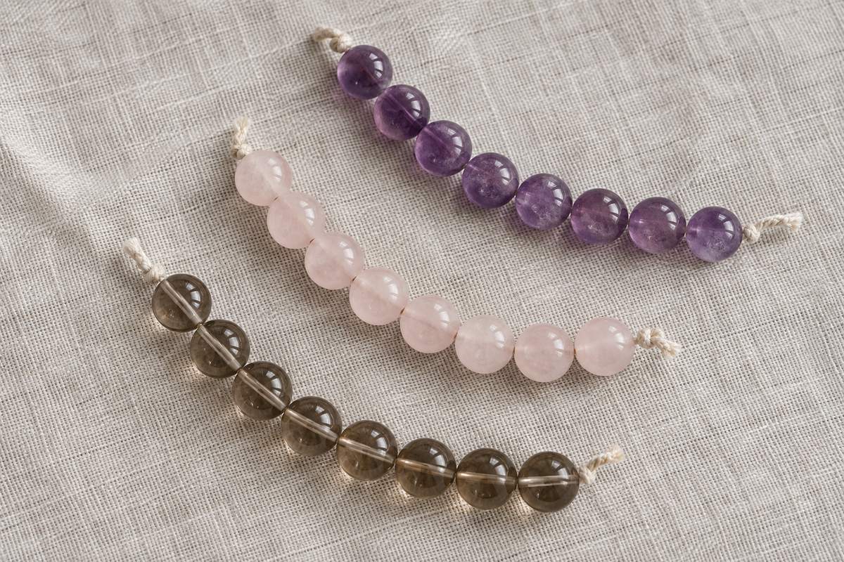 Purple, pale pink, and smoky brown bead strands lying loosely on linen.