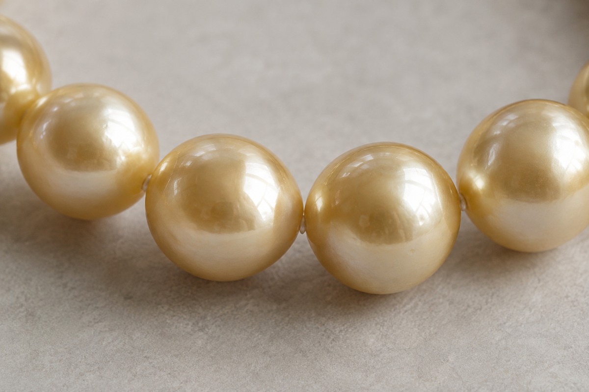 Five golden pearls showing broad, soft reflections across their surfaces.