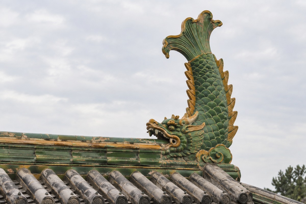 Tall green and yellow glazed ridge guardian above gray roof tiles