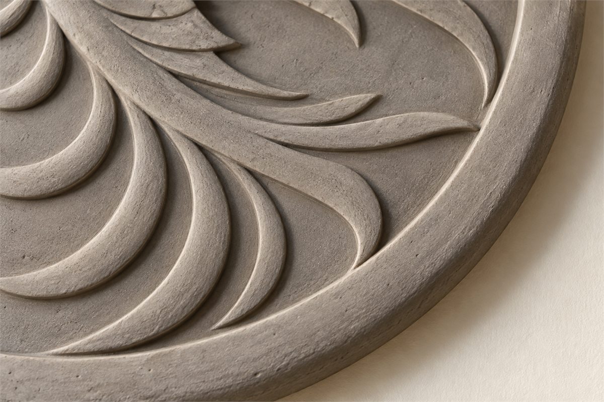Close view of a clay bird relief with a raised circular rim and open areas between feathers.
