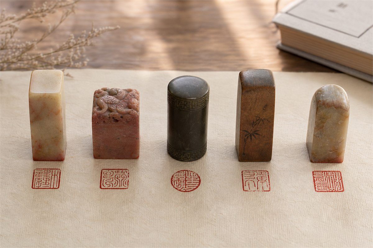 Five traditional stone and wood seals displayed with red impressions
