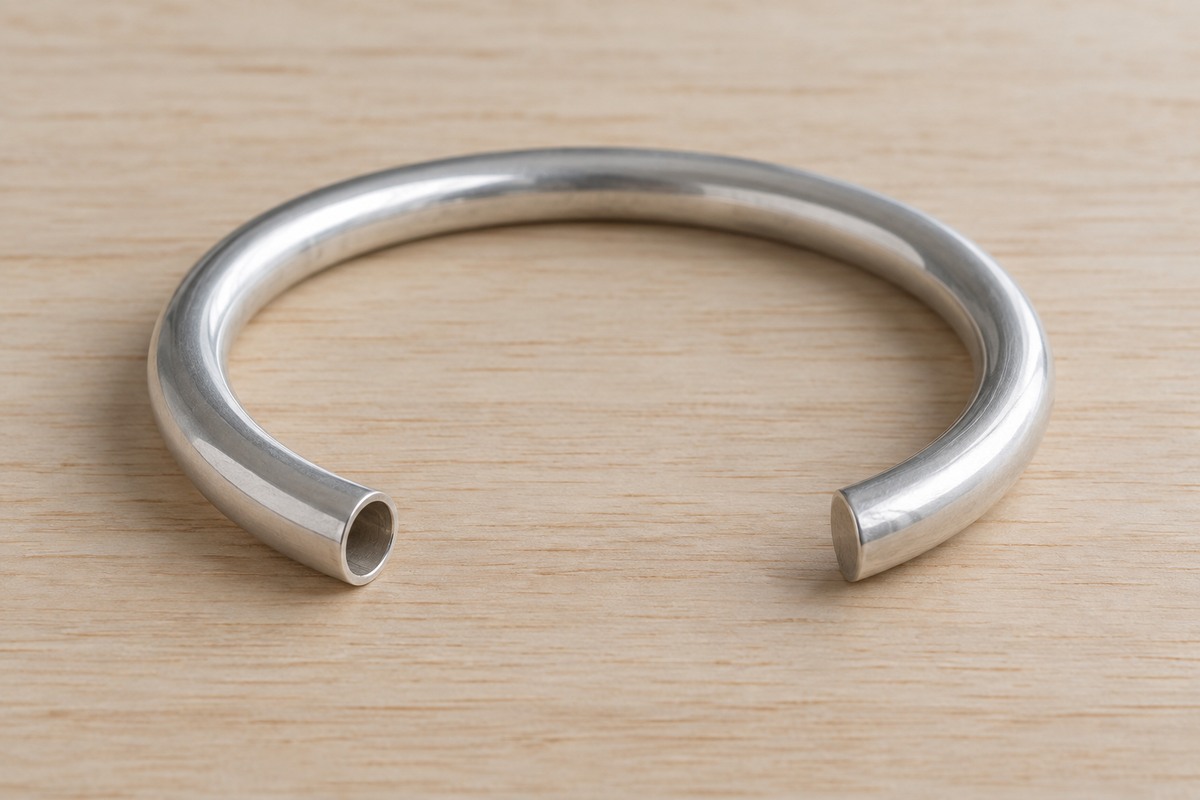 An unfinished tubular silver cuff with one open tube end and one capped end on a pale work surface.