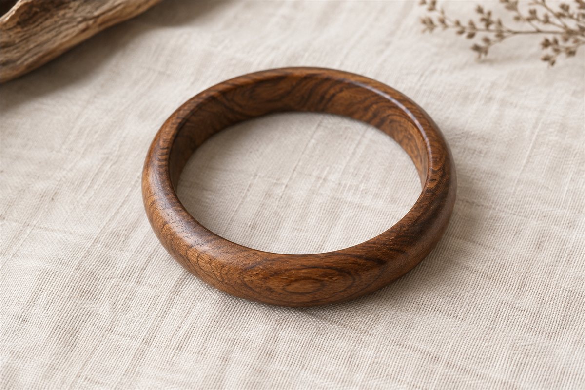 A smooth brown wooden bangle lies flat on ivory linen, showing its uninterrupted round outline.