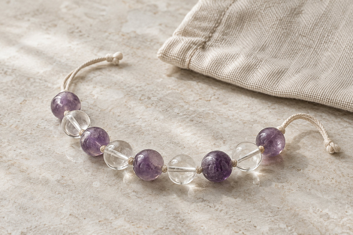 Violet and clear beads in a gently curved strand beside a linen pouch