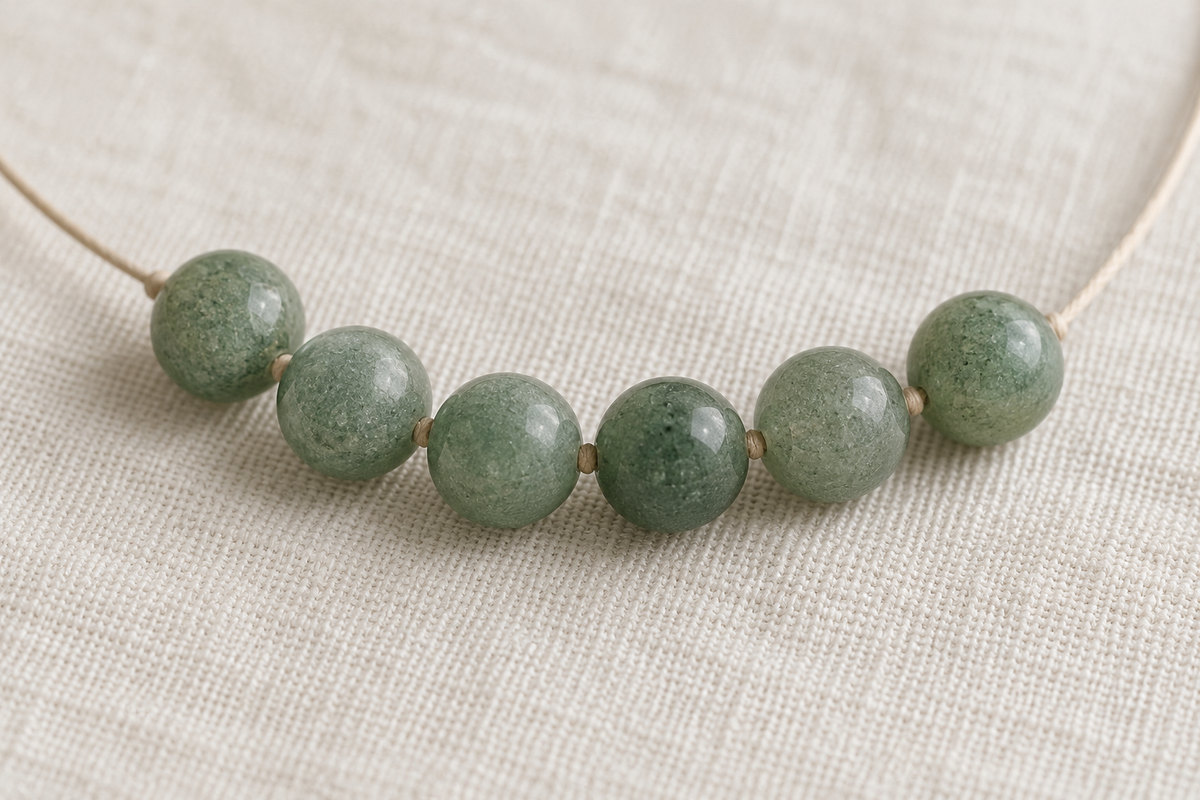 Soft green beads with fine reflective flecks on woven ivory cotton