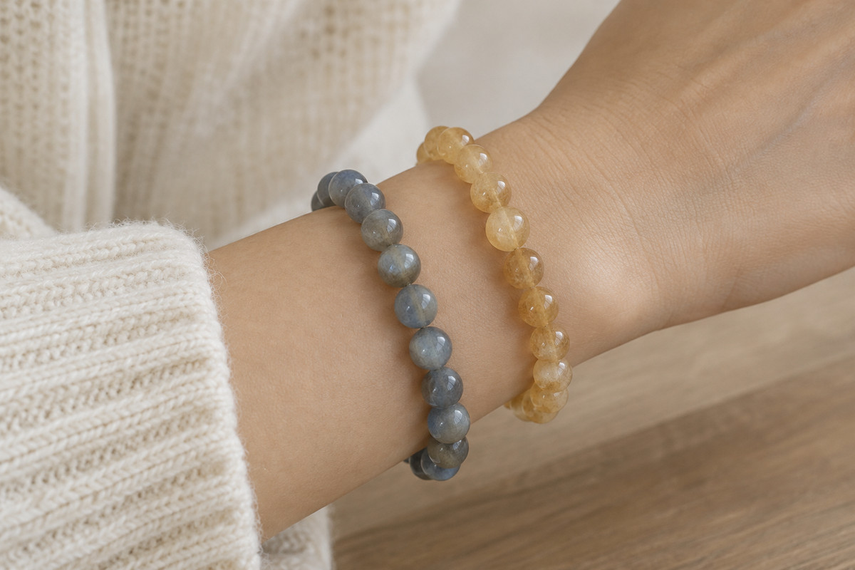 A forearm wearing two separated bead bracelets beside an ivory sleeve