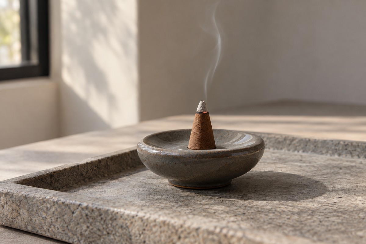 A small grey-tipped cone with a subtle red ember and a faint wisp on a heatproof seat.